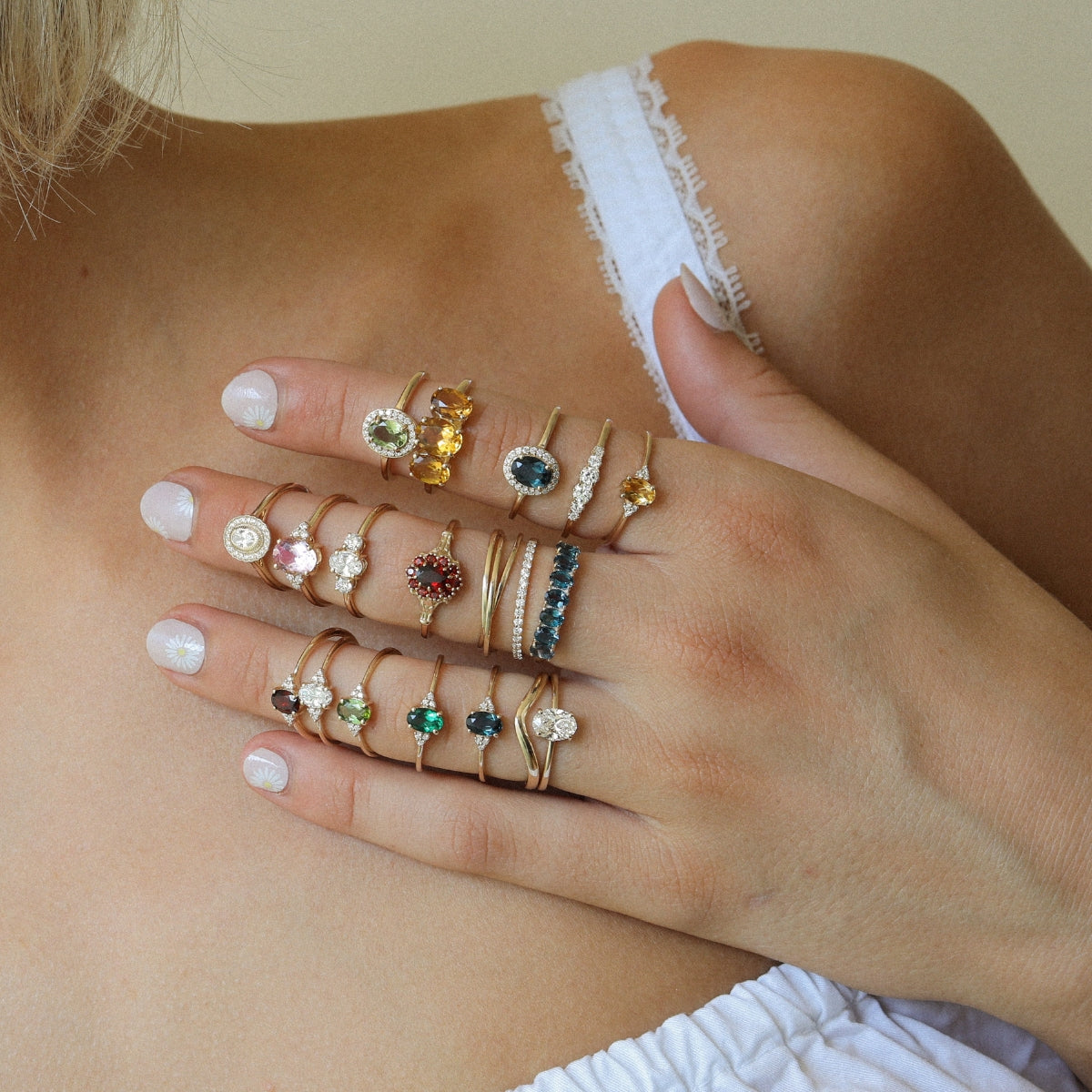 Hand met een collectie 9K en 14K gouden ringen met diamanten en kleurrijke edelstenen, gedragen als stijlvolle ring stack.