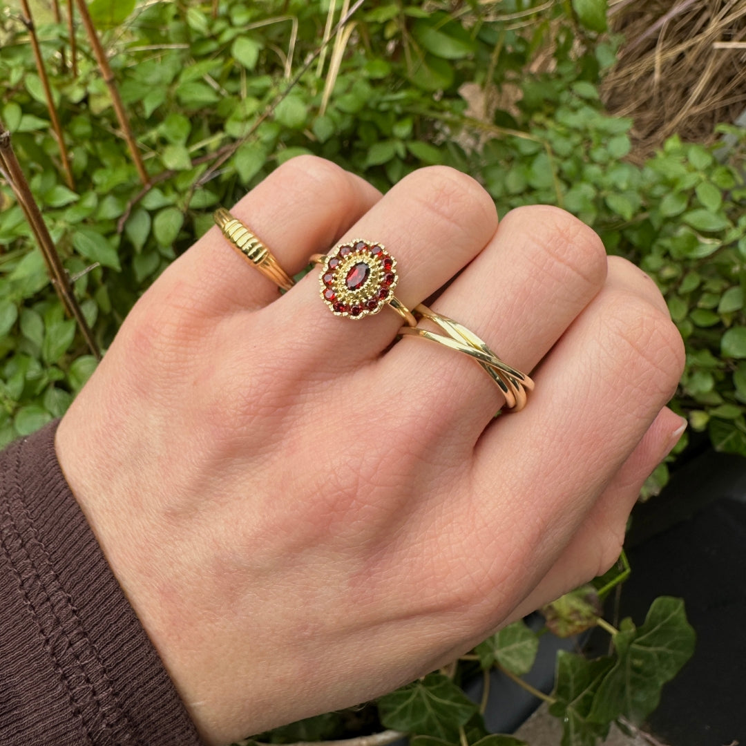 Hand met een goudkleurige ring met rode granaatstenen, gecombineerd met andere gold plated ringen – elegante en tijdloze sieradenstijl.