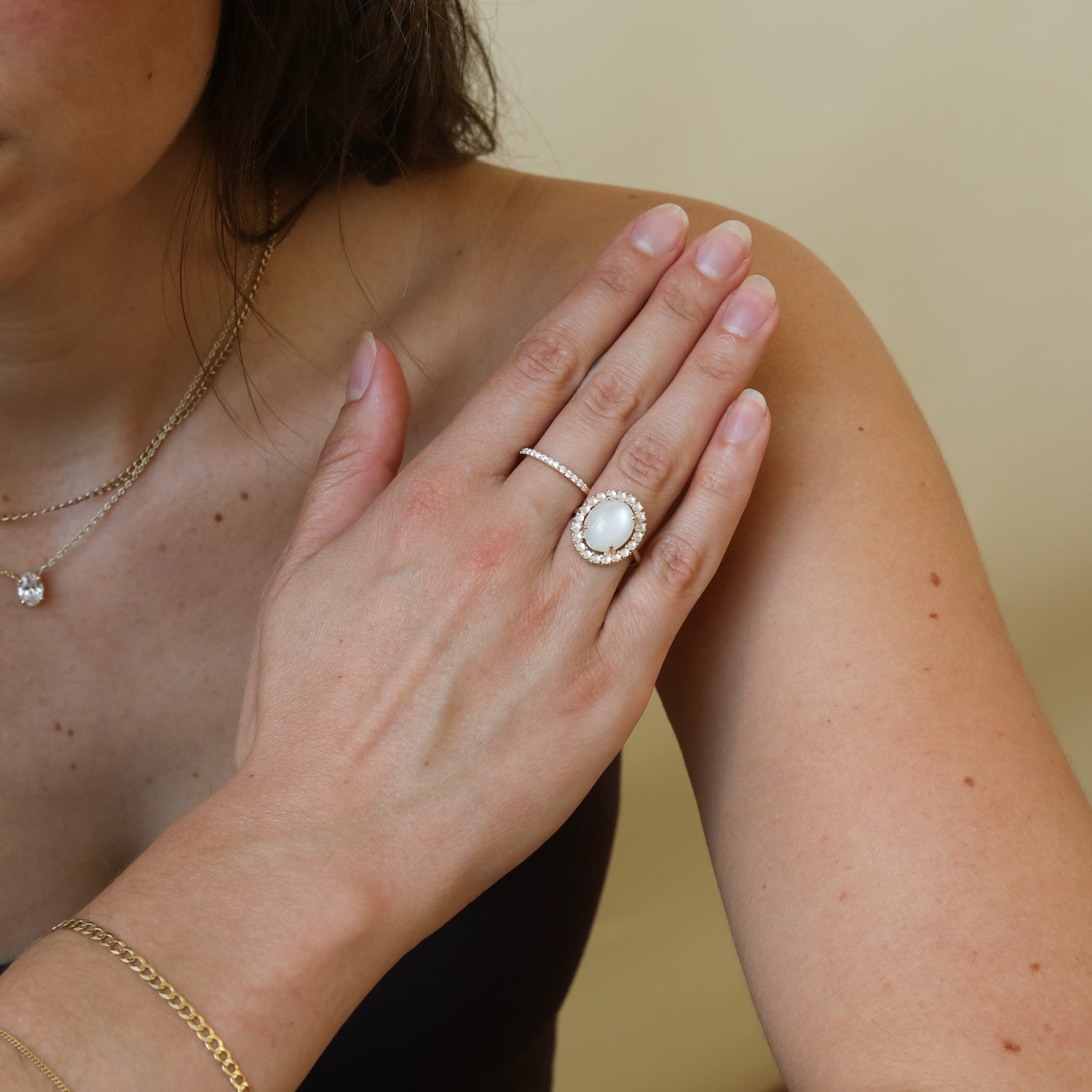 Model draagt de Livia Moonstone Halo Ring van 9 karaat goud met een grote maansteen, omringd door een halo van kleinere maanstenen.