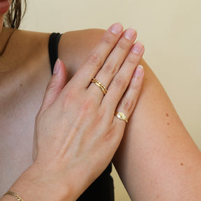 Close-up van de Nora Round Signet Ring van gold plated brass, gecombineerd met de Mae Vintage Stacking Ring.
