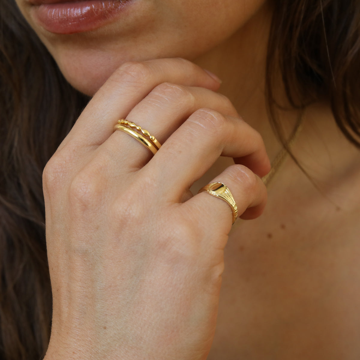 Model draagt de Nora Round Signet Ring van gold plated brass met een ronde bovenzijde voor een persoonlijke gravering van een initiaal.