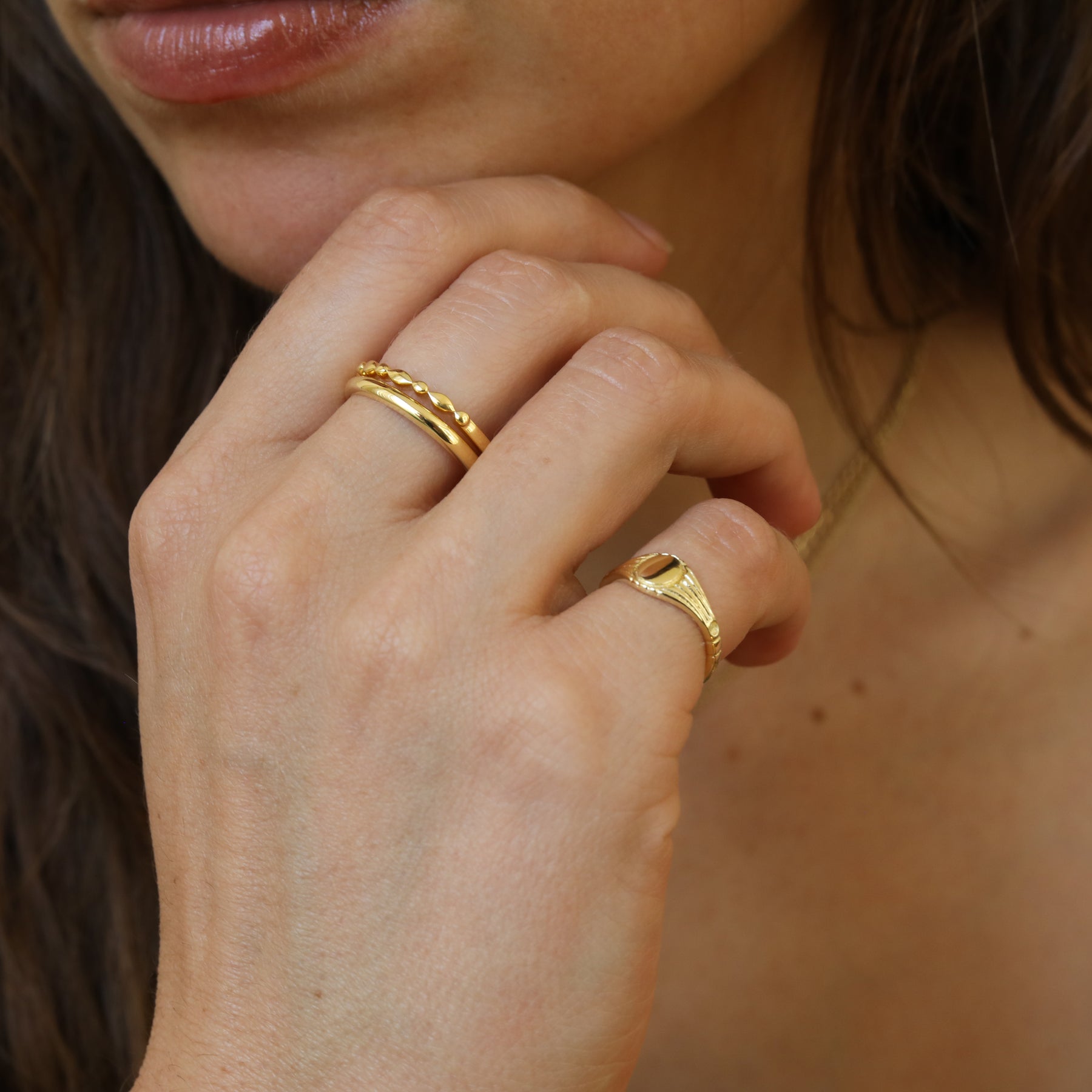 Model draagt de Nora Round Signet Ring van gold plated brass met een ronde bovenzijde voor een persoonlijke gravering van een initiaal.