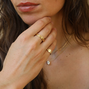 Model draagt de Tiara Octagon Signet Ring van gold plated brass met een gegraveerde initiaal op de achthoekige zegelring.
